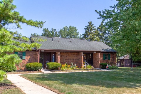 the front of a brick house with a lawn and trees