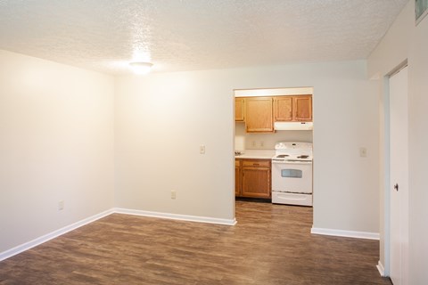 an empty living room and kitchen with wood flooring and white walls