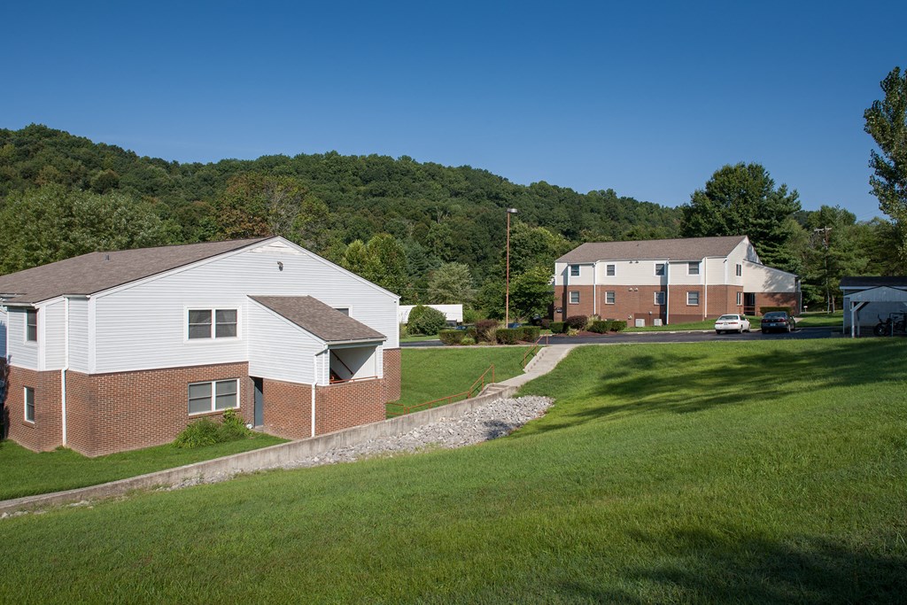 an aerial view of two houses with a hill and trees in the background