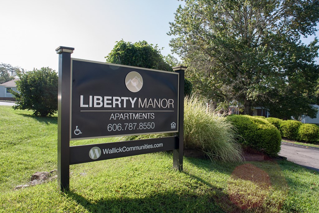 a sign for liberty manor apartments in front of a yard with grass and trees