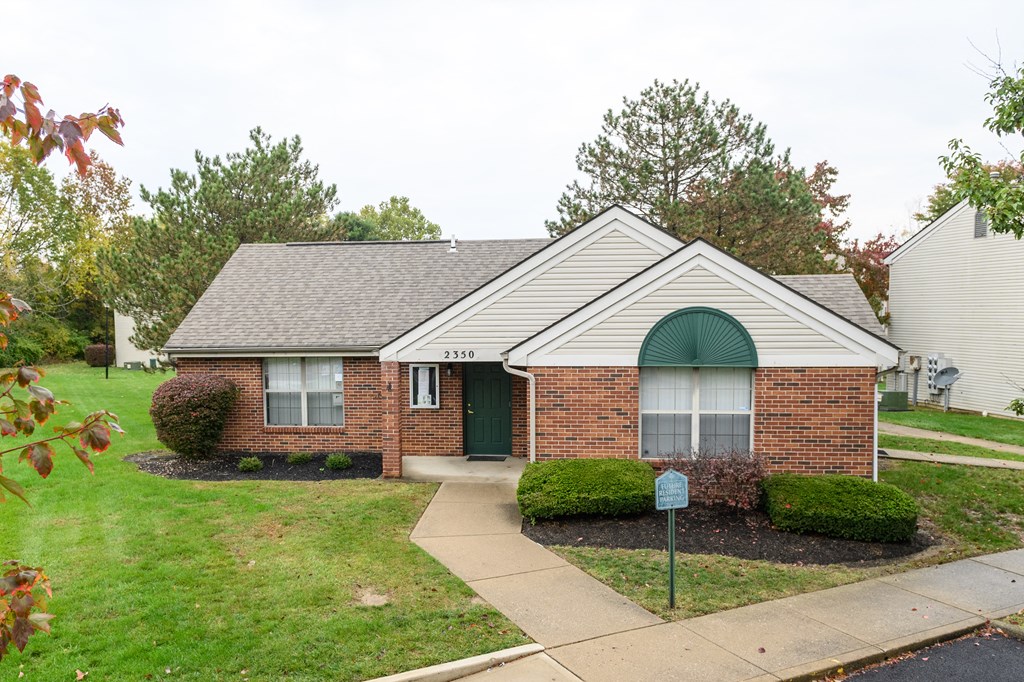 the front of a brick house with a lawn and a sidewalk
