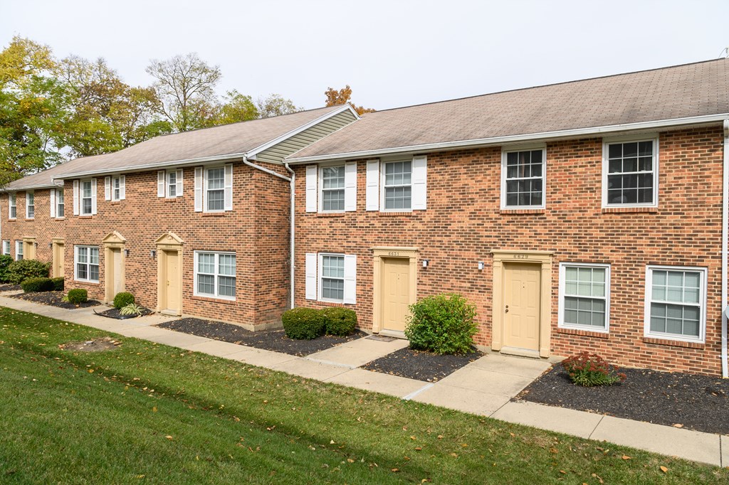 a brick apartment building with yellow doors and a sidewalk