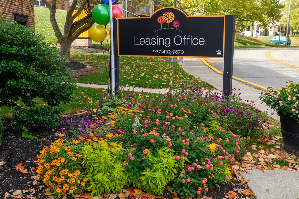 a sign for leasing office in front of a flower garden