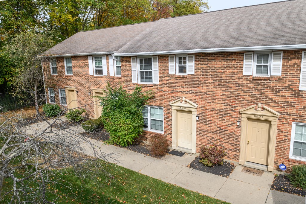 the front of a brick house with yellow doors and a sidewalk
