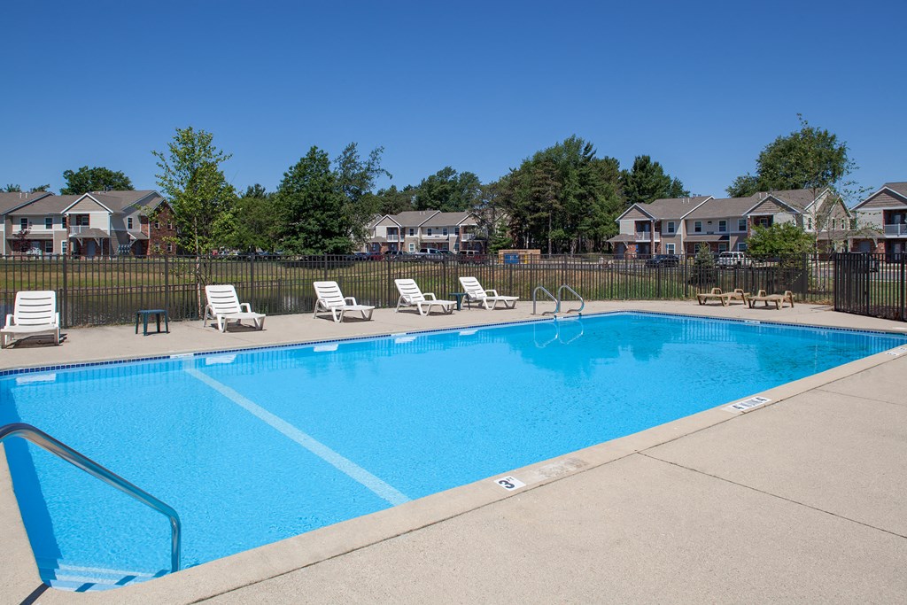 a swimming pool with chairs and a fence with houses in the background