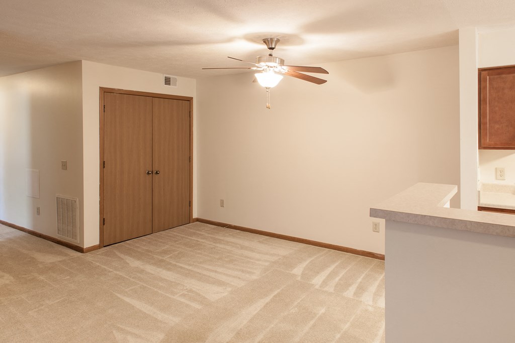 an empty living room with a ceiling fan and a door to a closet