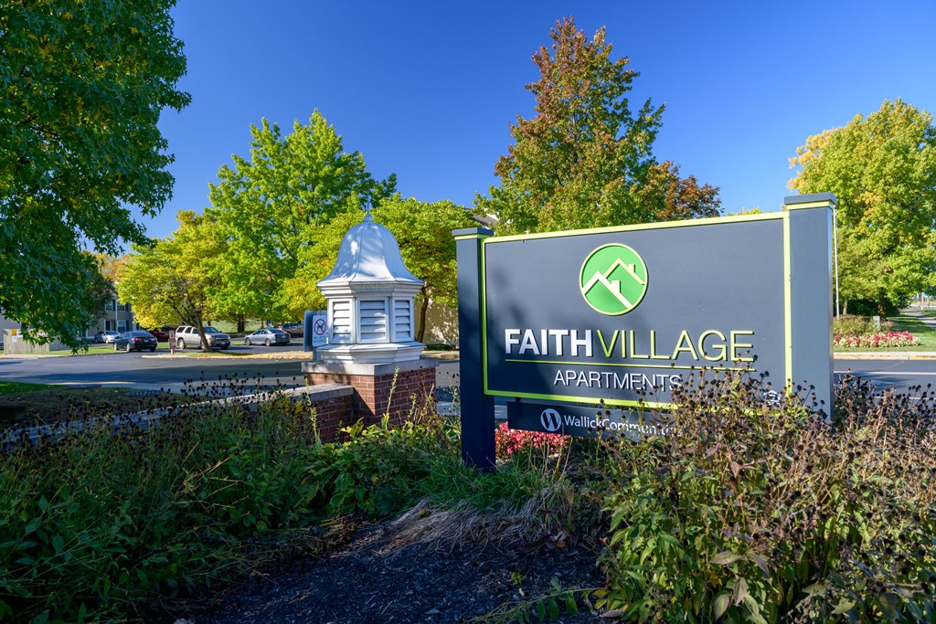 a sign for faith village in front of a park with trees