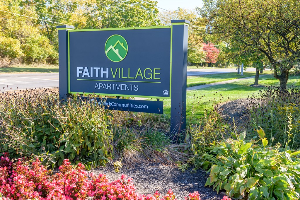 a sign for faith village apartments in front of flowers
