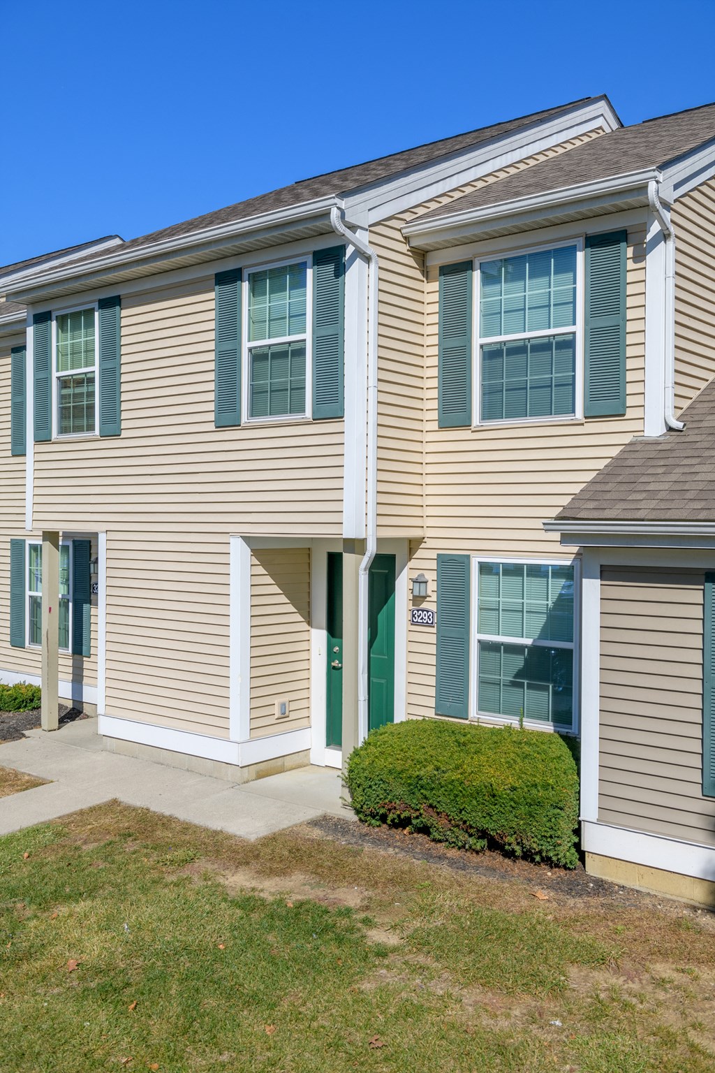a building with tan siding and green shutters and a green lawn