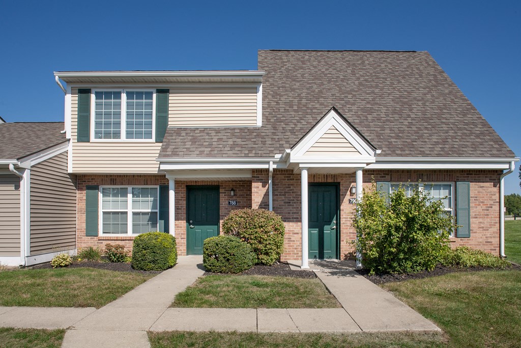 a brick house with green doors and a sidewalk