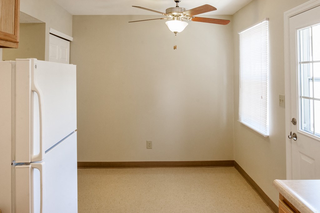 an empty kitchen with a refrigerator and a ceiling fan