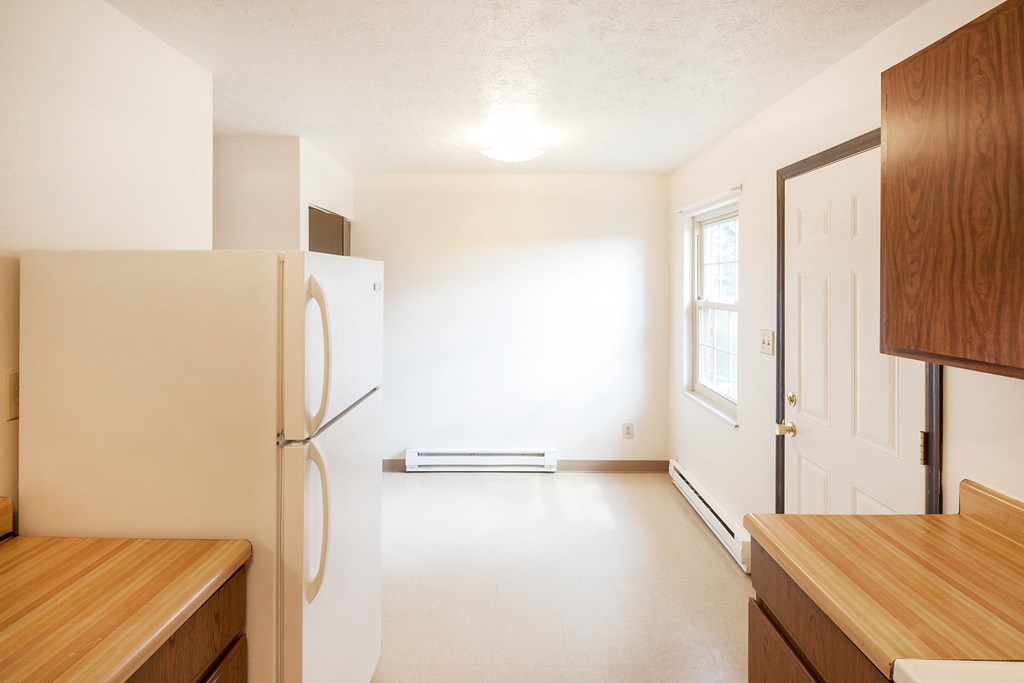 an empty kitchen with a refrigerator and wooden cabinets