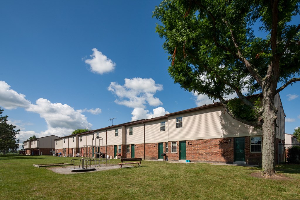A tree stands in front of a building with a playground in the foreground.