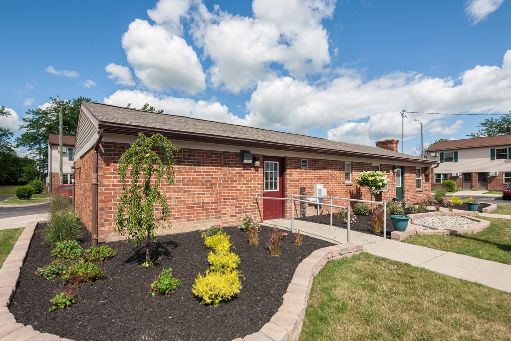 the front yard of a brick house with a garden and a sidewalk