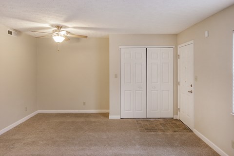 an empty living room with a ceiling fan and a closet