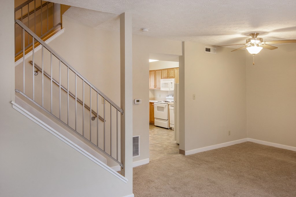 an empty living room with a staircase and a kitchen in the background