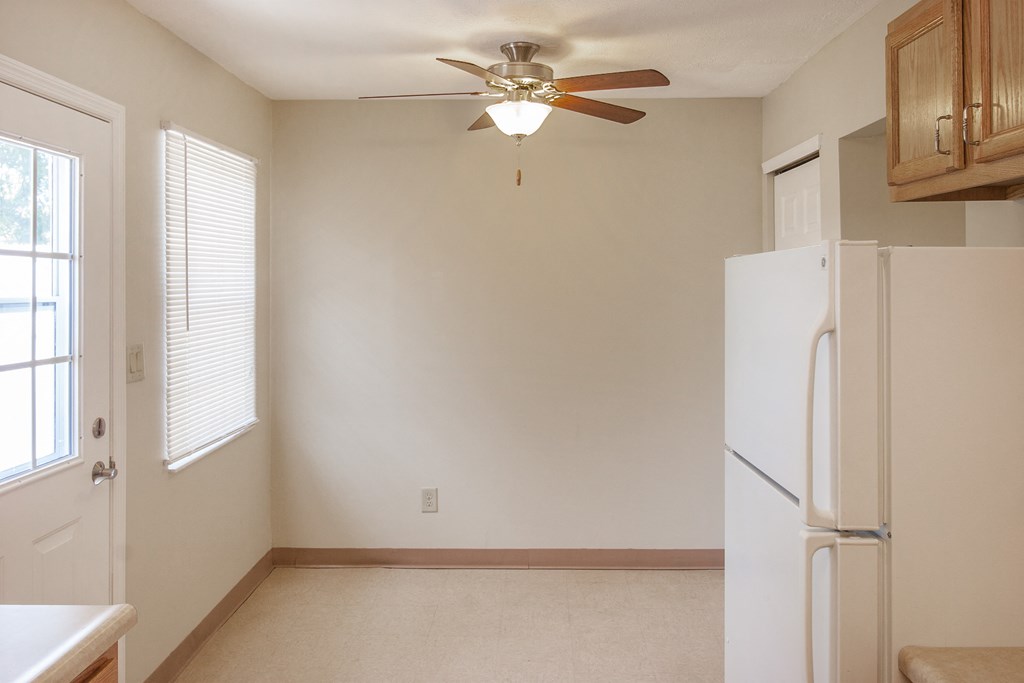 an empty kitchen with a refrigerator and a ceiling fan