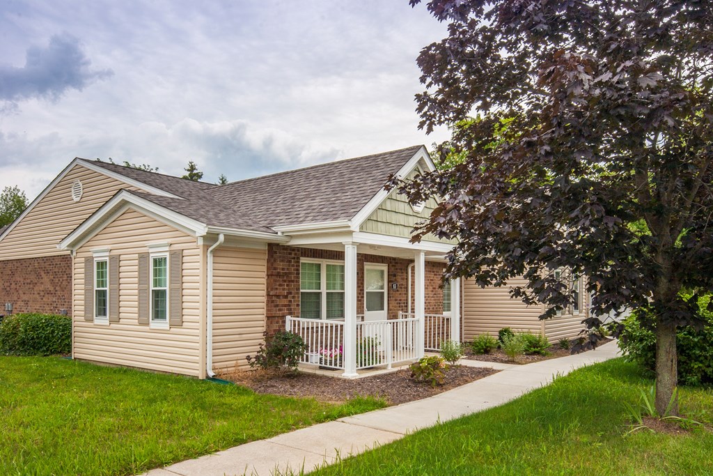 a small tan house with a porch and a tree