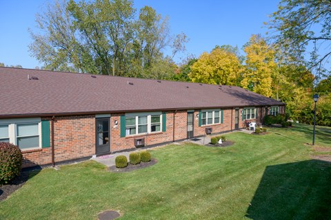 the front of a brick house with a lawn and trees