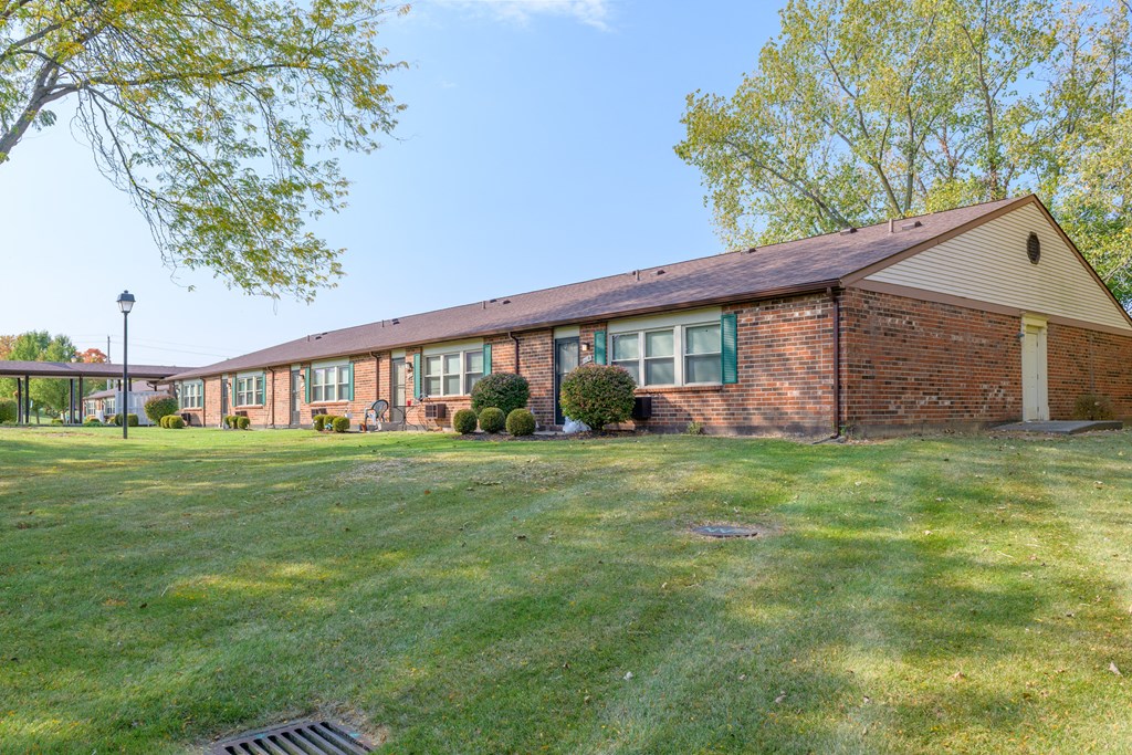 the front of a brick building with green grass and trees