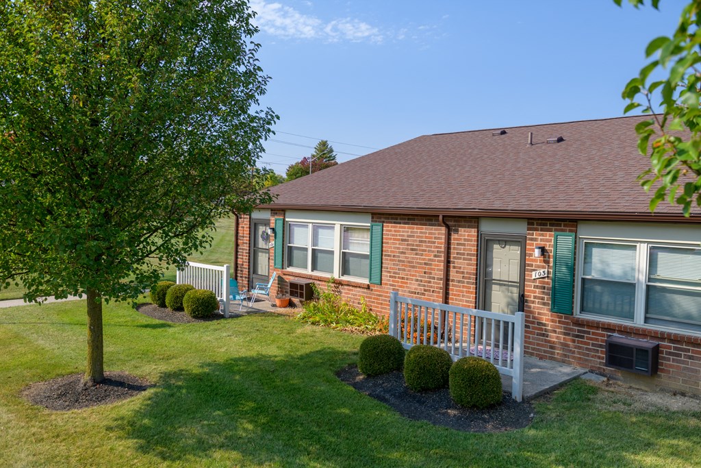 the front of a brick house with a porch and a tree
