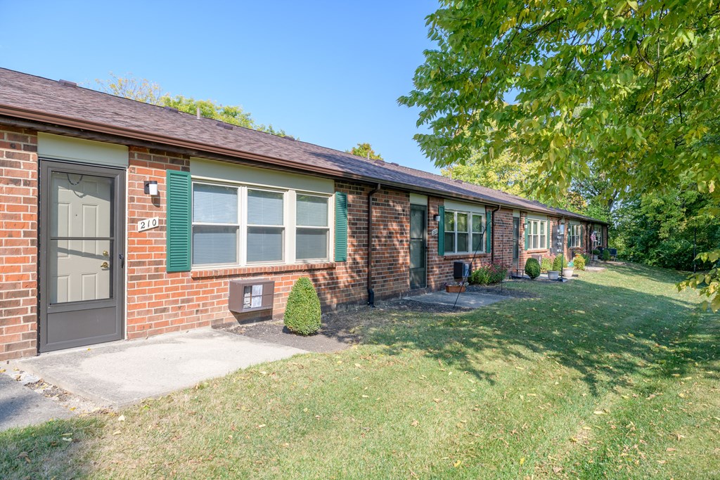 the front of a brick house with green shutters and a lawn