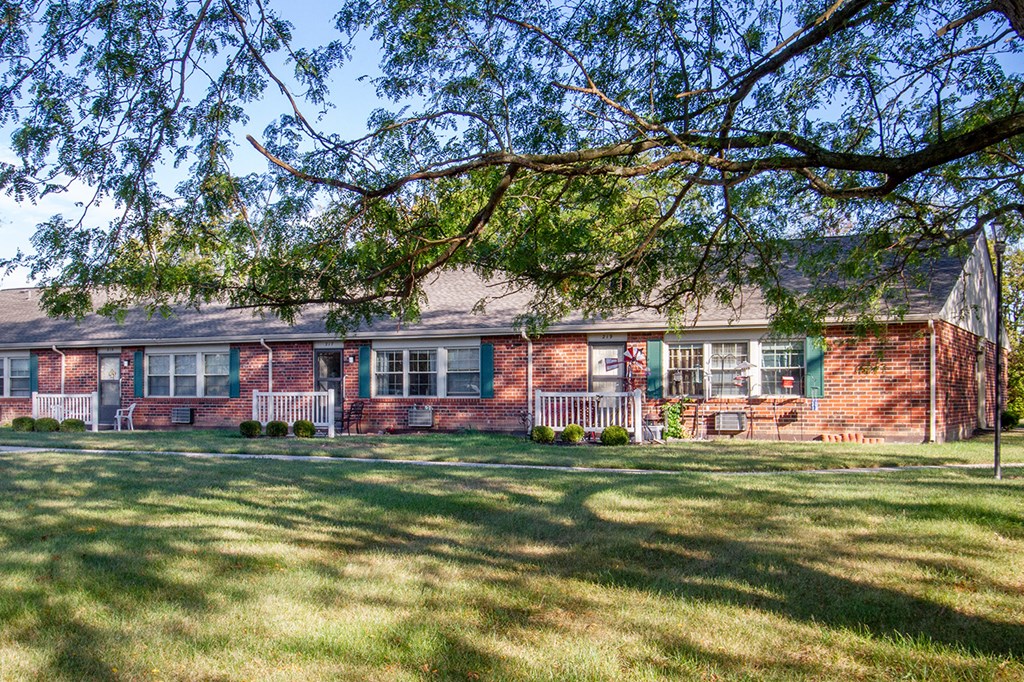 the front of a brick house with a yard and a tree