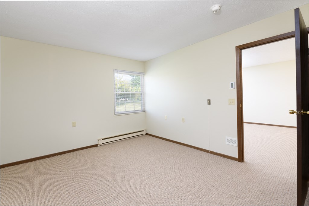 a bedroom with white walls and carpet and a door open
