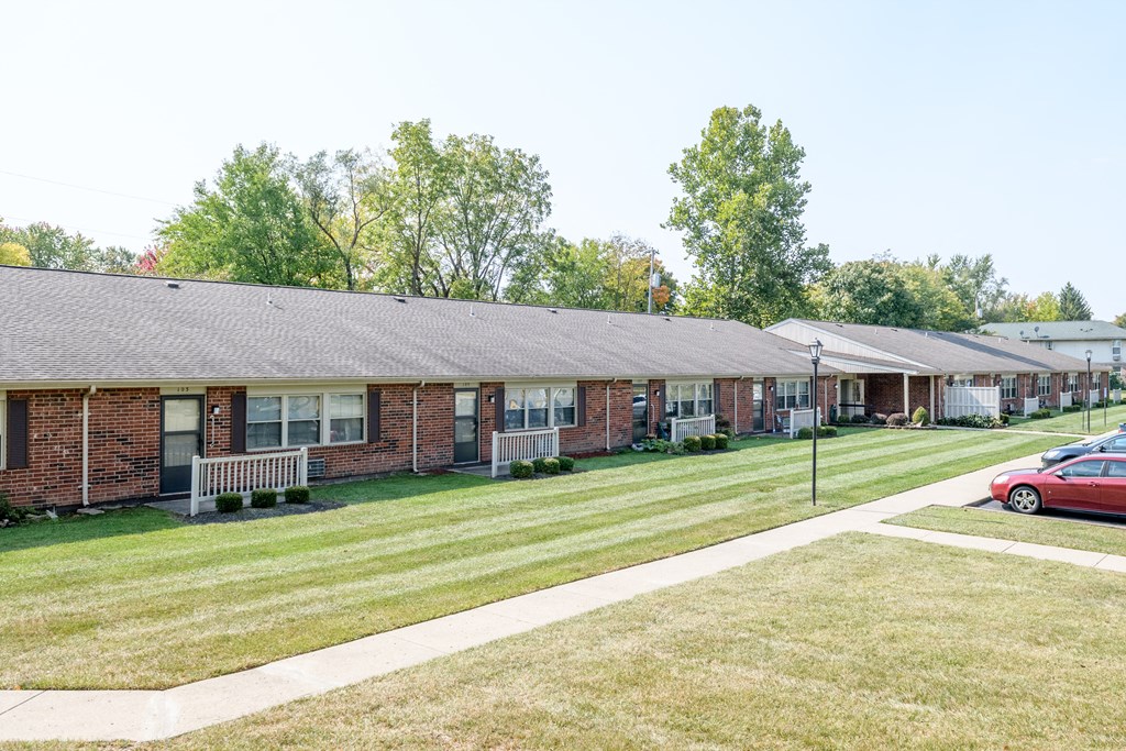 a row of brick apartment buildings with a lawn and cars parked in front