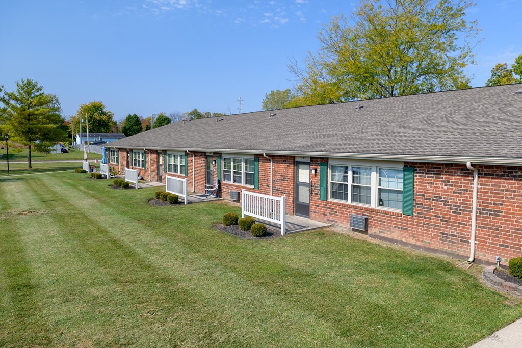 the front of a brick building with a lawn and a porch
