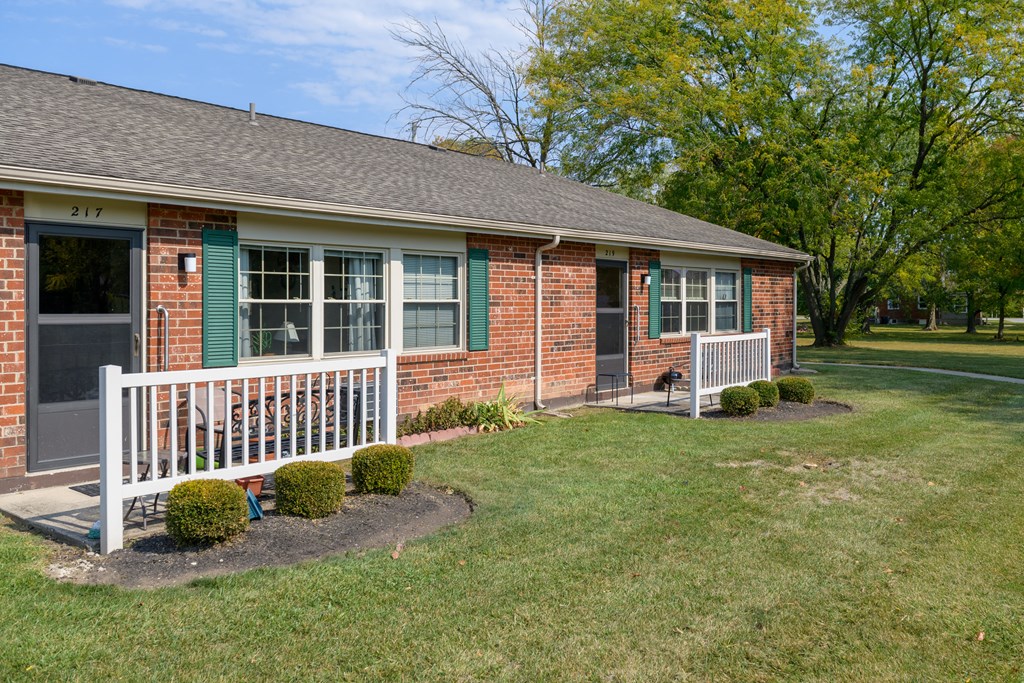 a small brick house with a white porch and green shutters