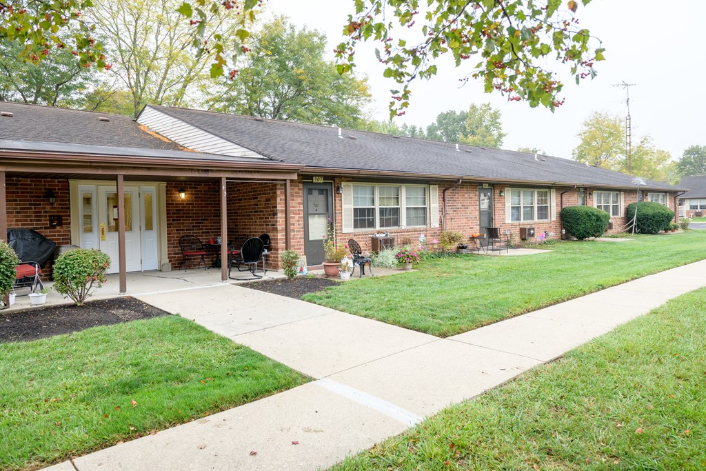 the front of a brick house with a lawn and a sidewalk