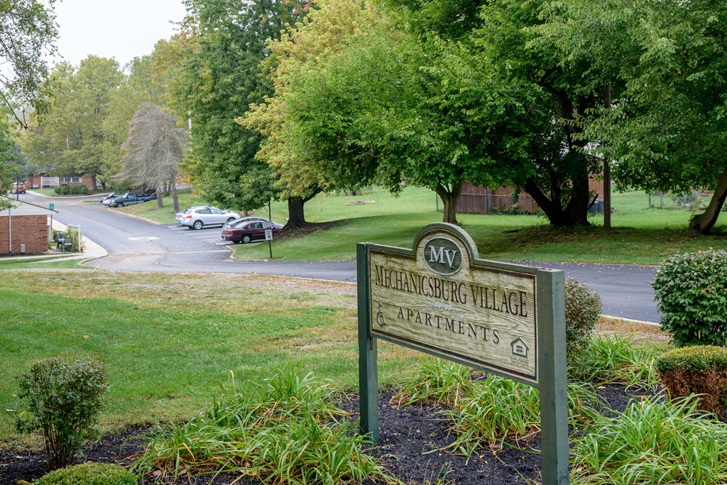 a sign in front of a park on the side of a street