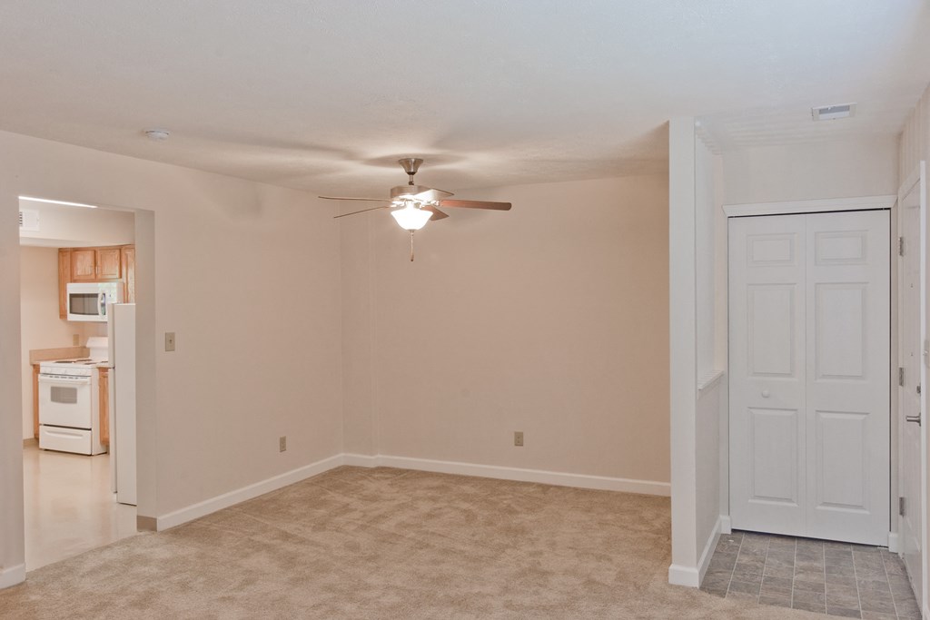 an empty living room with a ceiling fan and a kitchen