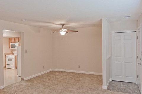 an empty living room with a ceiling fan and a kitchen