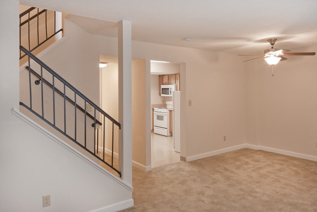 an empty living room and kitchen with a ceiling fan and a staircase