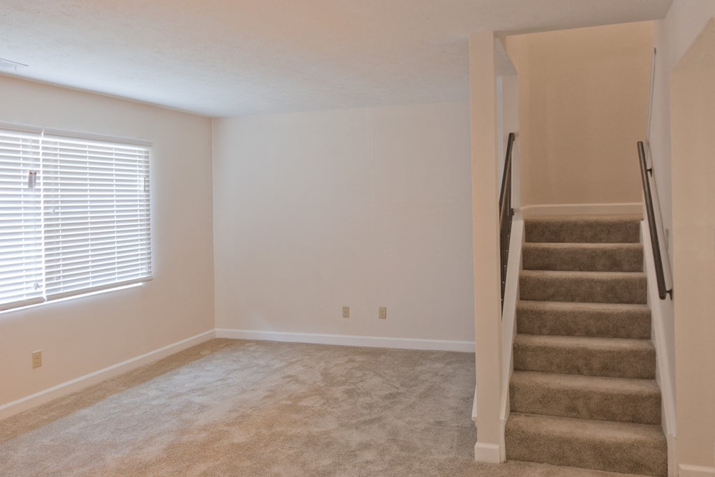 an empty living room with a staircase and a window