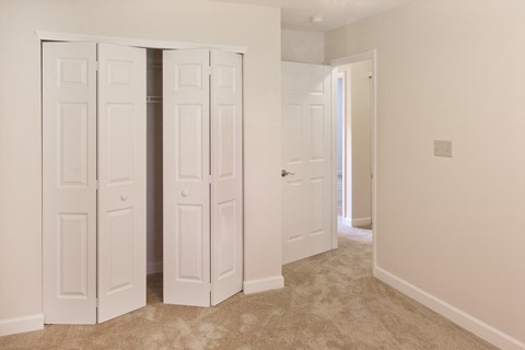 an empty bedroom with white closets and a carpeted floor