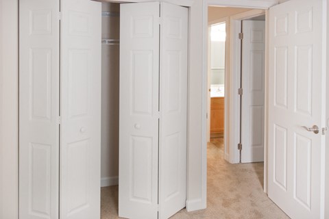 a row of white closet doors in a room with a bathroom in the background