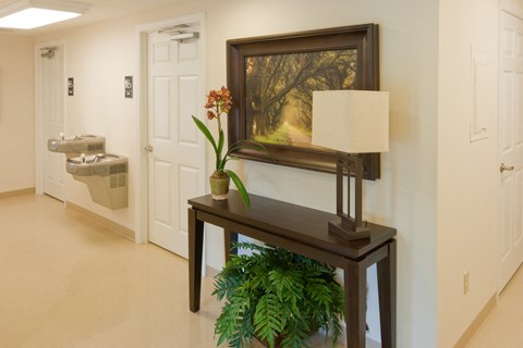 a hallway with a table with a lamp and a painting on the wall