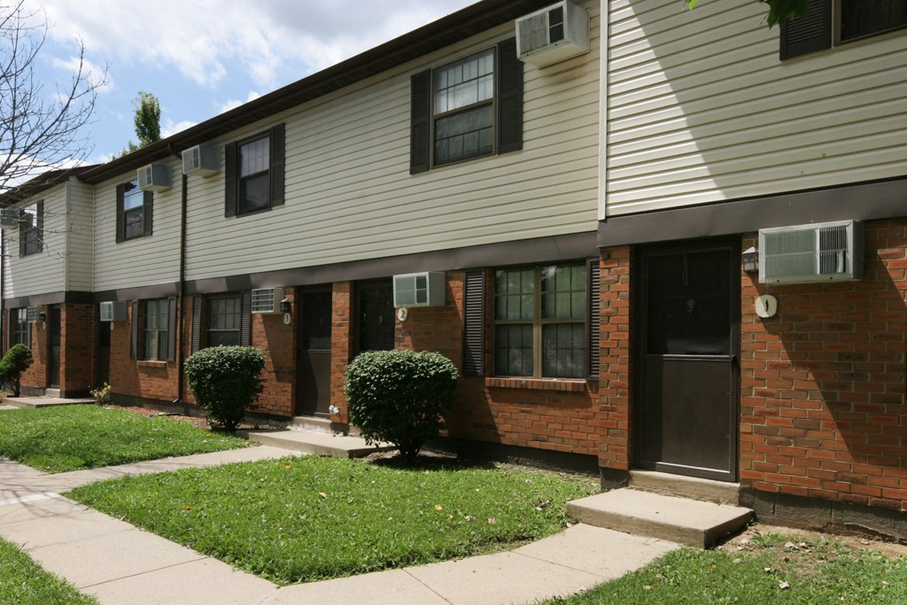 a brick and white building with a sidewalk and grass