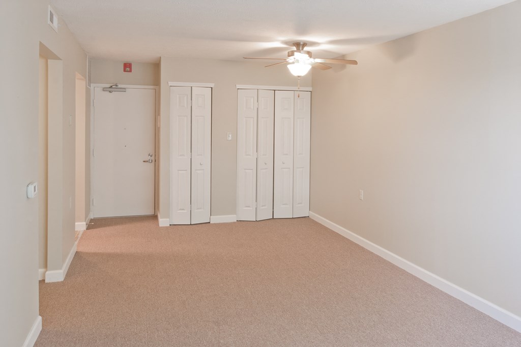 an empty living room with a ceiling fan and white closets