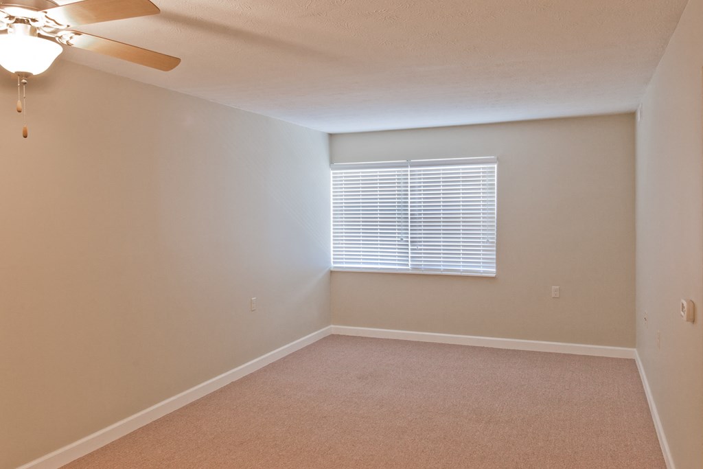 an empty bedroom with a window and a ceiling fan