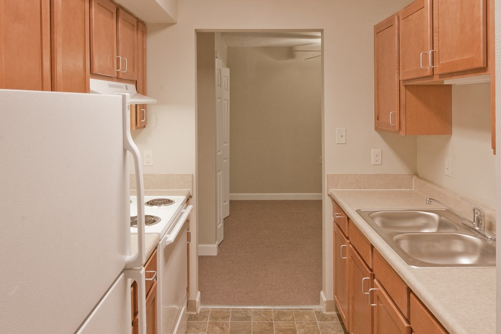 a kitchen with white appliances and wooden cabinets and a door to a hallway
