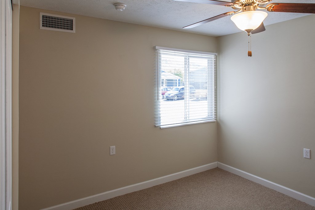 an empty bedroom with a window and a ceiling fan