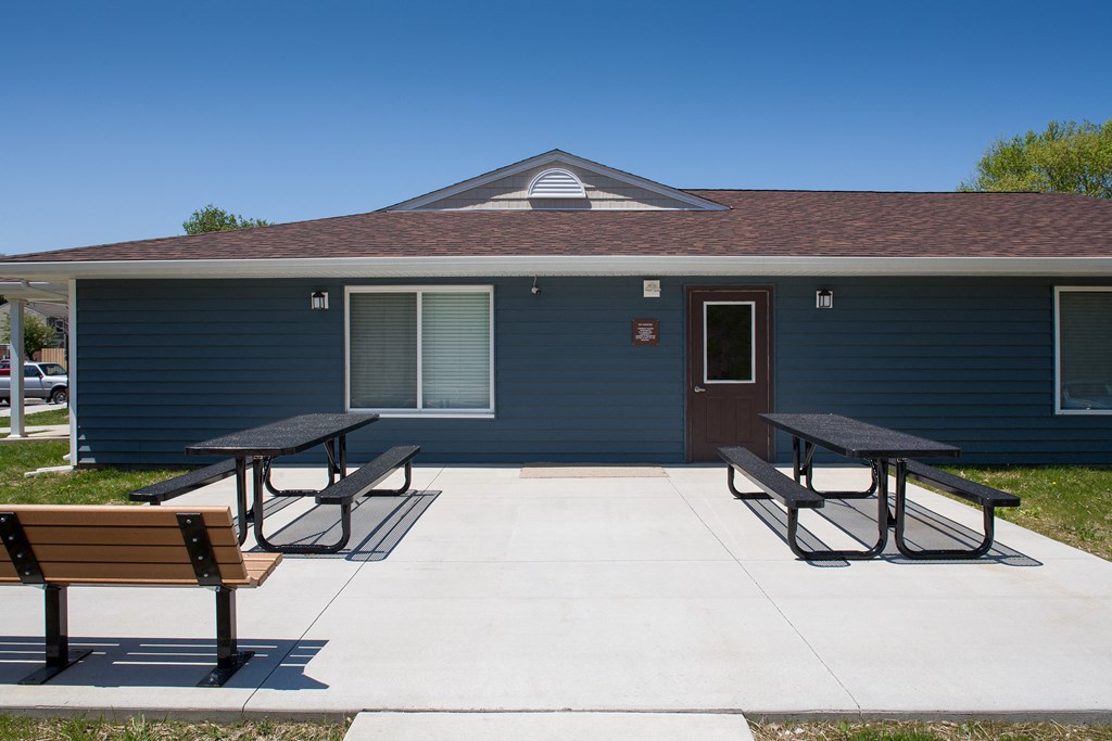 a patio with two picnic tables in front of a blue building