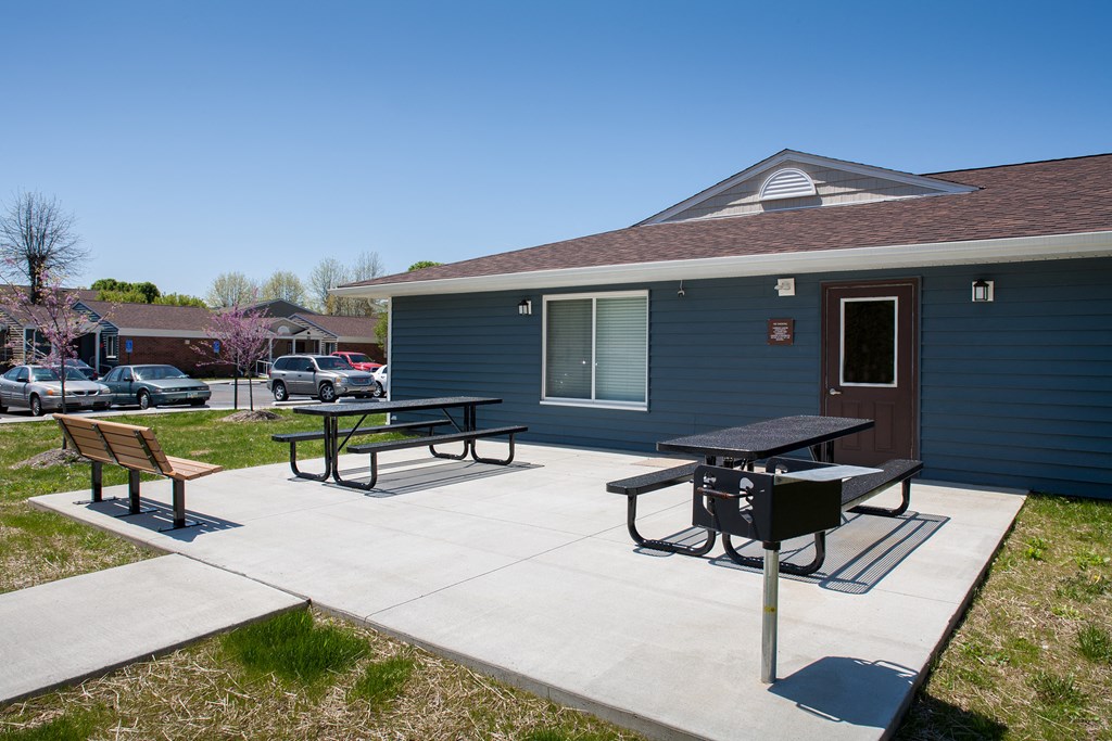 a patio with two picnic tables in front of a blue building