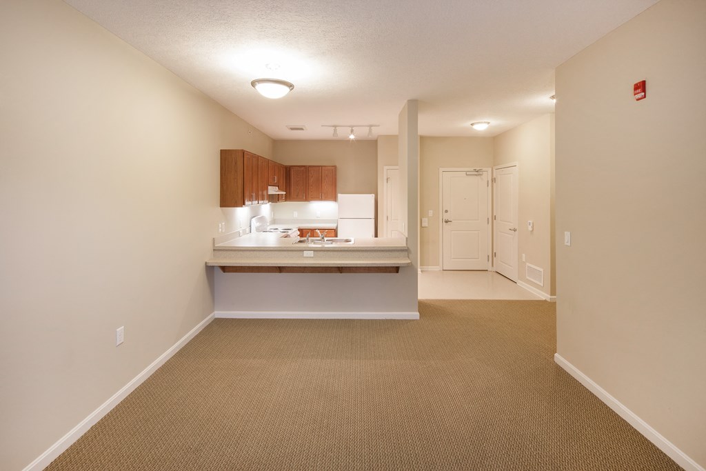 an empty kitchen and living room with carpeting and a hall way to a door