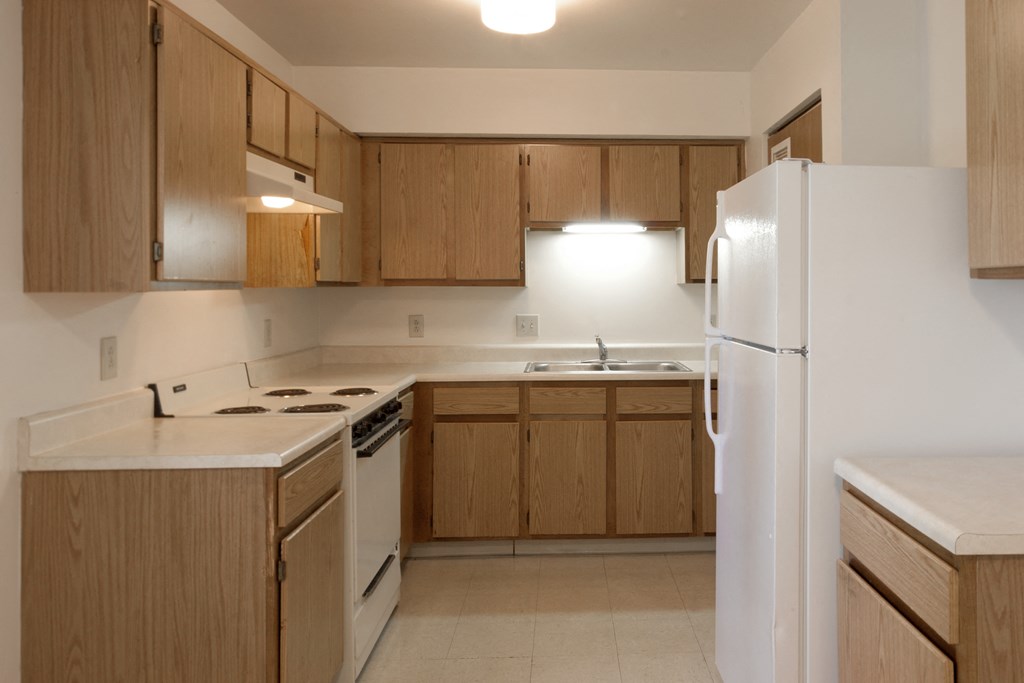 an empty kitchen with white appliances and wooden cabinets