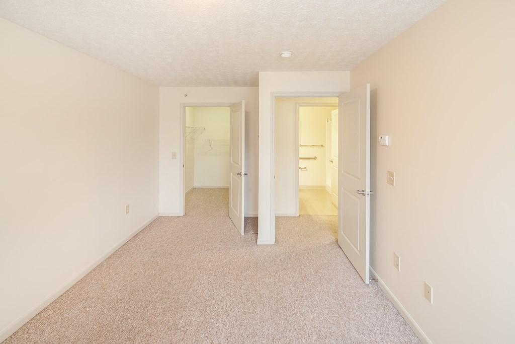 a spacious living room with carpeting and a hallway to a bedroom